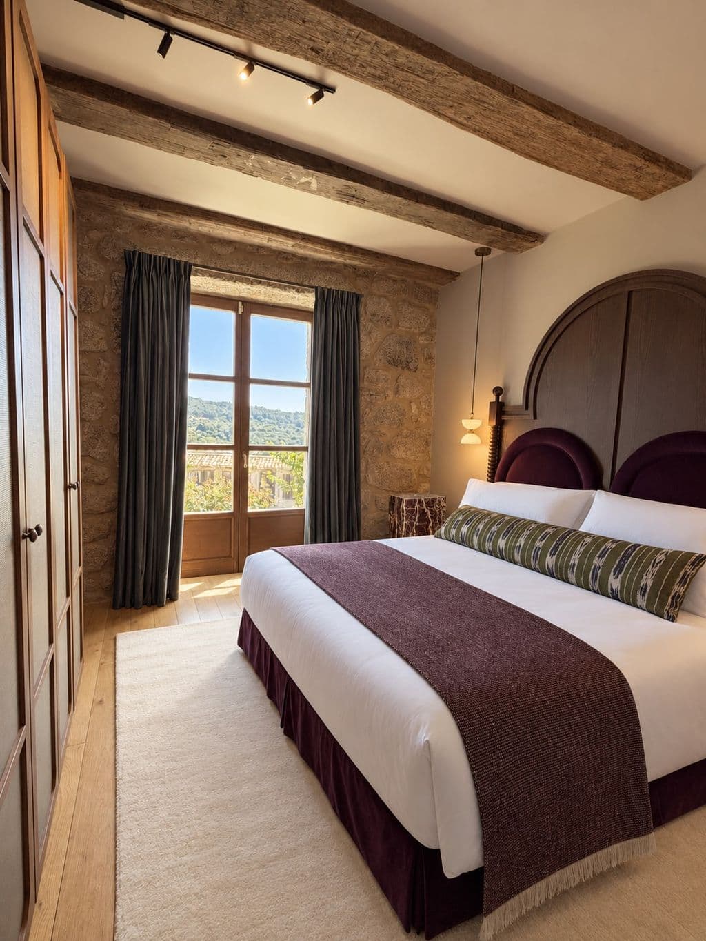 A bedroom beneath chestnut beams, with a deep-set window onto the valley
